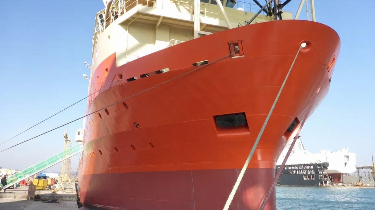 An offshore support vessel lying alongside a quay, seen from ahead, with mooring lines running down to the bollards.